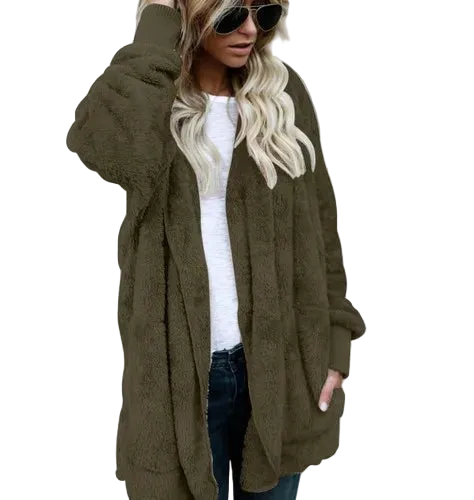 Person wearing an olive green cardigan over a white top and dark jeans against a gray concrete wall.