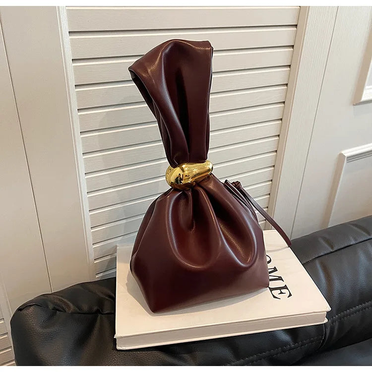 Brown leather bag with gold clasp on a book against a neutral background