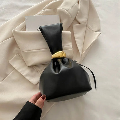 Black handbag with gold clasp held by a hand on a light beige fabric background