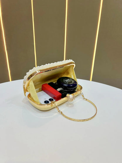 Gold Carauana Pearl Clutch Purse capacity with makeup items on a white surface and gold background