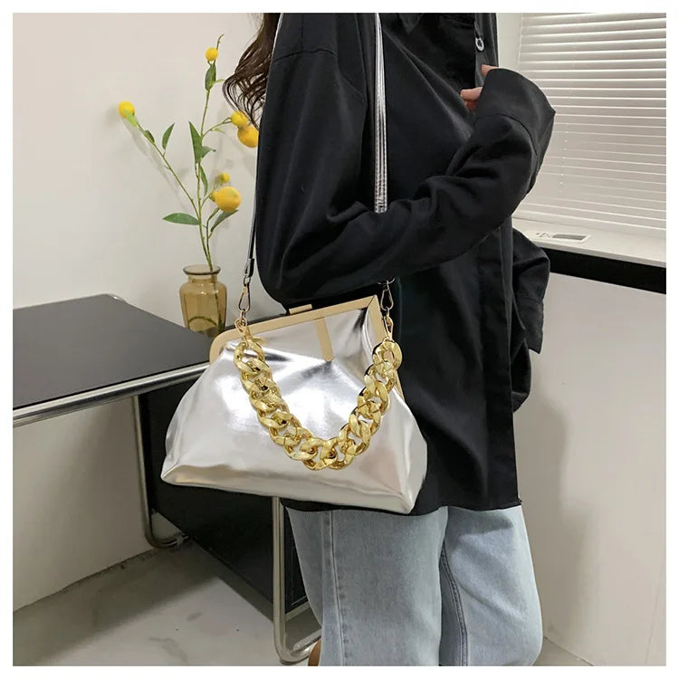 Person holding a silverCarauana UNIU Aurora Clutch handbag with a gold chain strap in an indoor setting.