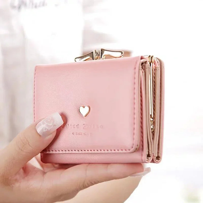 Pink wallet with a heart design held by a hand against a white background