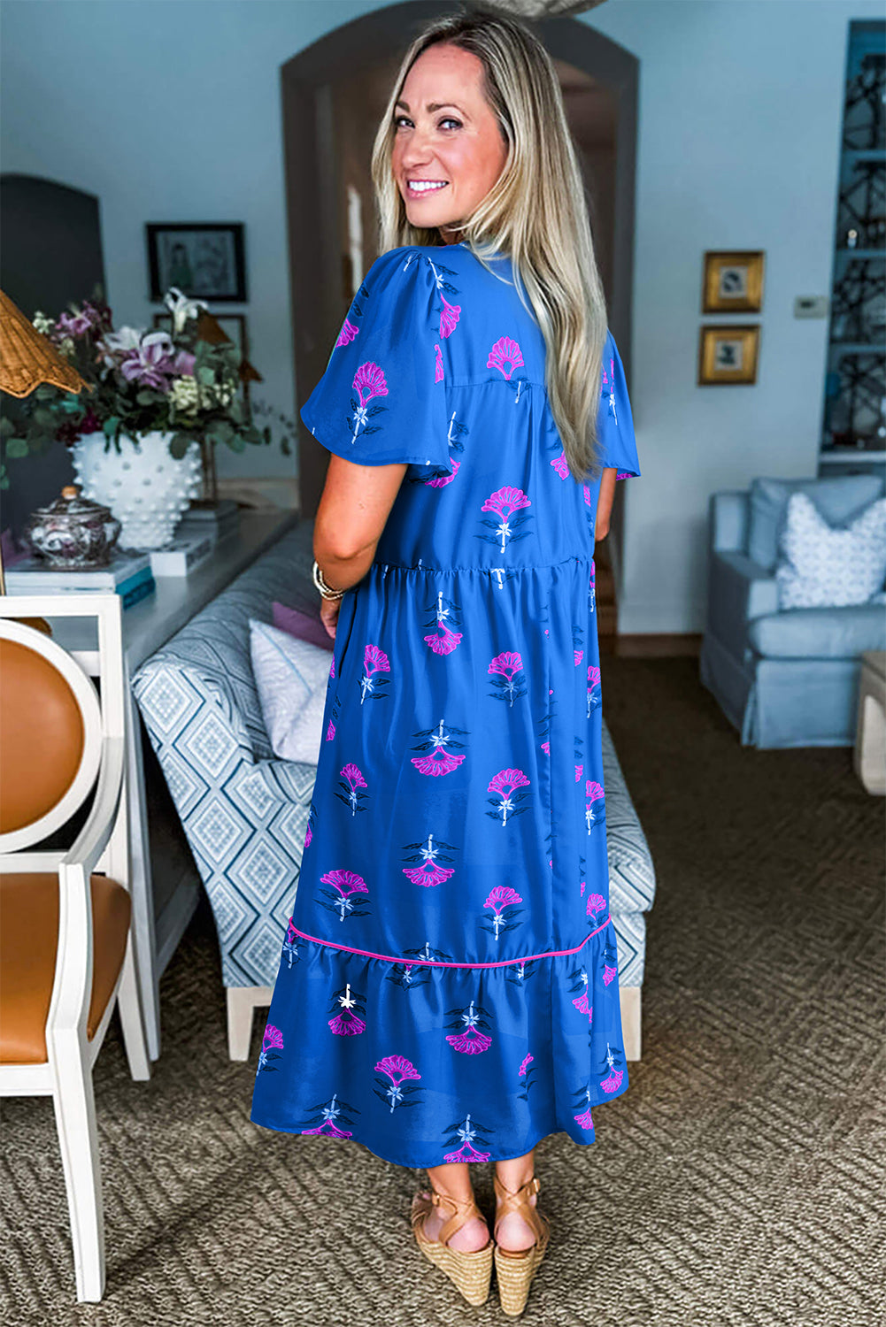 Woman wearing a blue dress with pink floral patterns in a living room setting.
