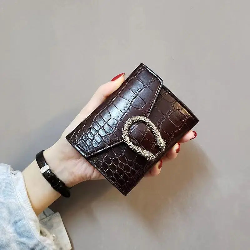 Hand holding a brown crocodile-patterned wallet with a decorative buckle black color